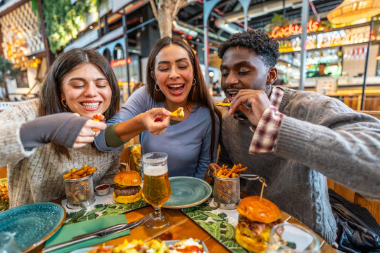 Happy multi ethnic friends eating nachos and burgers at restaurant