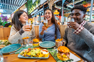 Happy multi ethnic friends toasting and enjoying food and drinks at restaurant