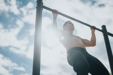 A shirtless man engaged in a fitness routine by doing pull-ups using a horizontal bar in an outdoor park, showcasing strength, focus, and determination on a sunny day.