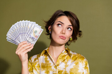 Confident young woman holding dollar bills against a khaki background, showcasing financial success...
