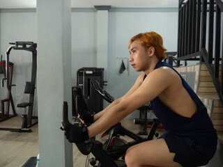 young sports indonesia asian man in blue cycling in fitness center. Cardio workout, leg workout,...