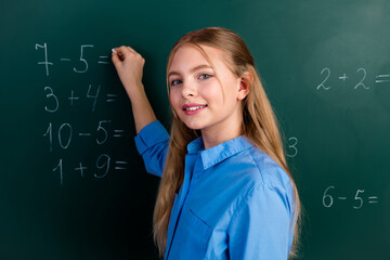 Schoolgirl solving math problems on chalkboard in classroom wearing blue shirt