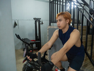 young sports indonesia asian man in blue cycling in fitness center. Cardio workout, leg workout,...