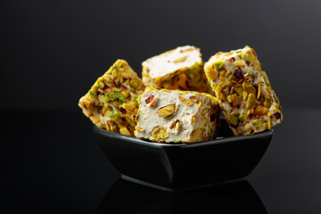 Turkish delight in a small black dish on a black reflective background.