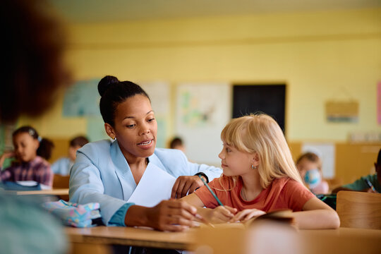 Black female teacher assisting schoolgirl during class at elementary school.