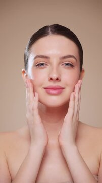 Beautiful Young Woman Touches Her Perfect Face. Natural Cosmetic Skincare Products. Woman demonstrate moisturizing facial care. Elevating Close-up vertical video. Slow motion