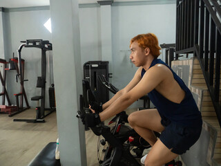 young sports indonesia asian man in blue cycling in fitness center. Cardio workout, leg workout,...
