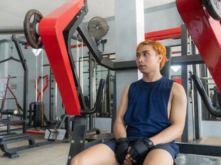 Fitness, breathing and sweat with tired asian indonesian man in the gym, resting after intense training. Training, health and fatigue with young athlete recovering from training for sports or fitness