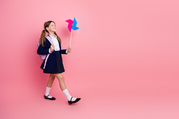 Charming Schoolgirl in Uniform Holding a Colorful Toy Pinwheel on a Pink Background, Smiling Happily