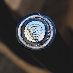 Cut power cable displaying aluminum conductor core surrounded by insulation and shielding used in energy transmission. Cross-section of thick electric cable revealing spiral arrangement of metal wires
