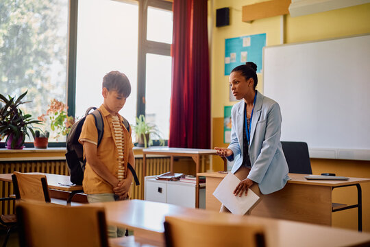 Worried African American teacher talking to her elementary student after class in classroom.