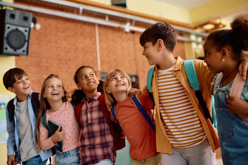 Group of happy diverse school kids standing embraced in hallway.