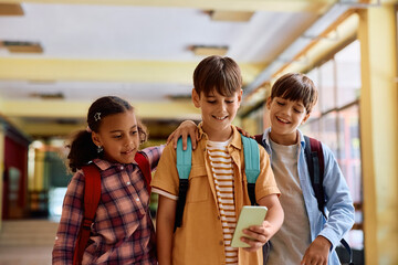 Multiracial group of elementary school classmates using cell phone in hallway.