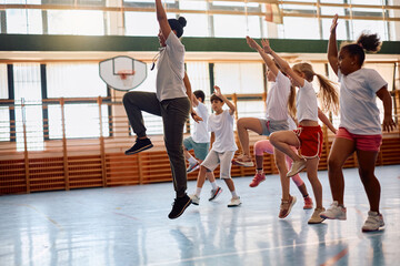 Black female PE teacher and elementary students exercising at school gym. © Drazen