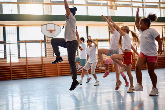 Black female PE teacher and elementary students exercising at school gym.