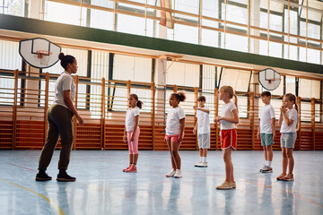 Fototapeta premium Black sports teacher and her students exercising during PE class at school.