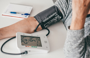 Elderly woman using medical device to measure blood pressure - senior woman suffering from hypertension sitting at home table taking care of her health