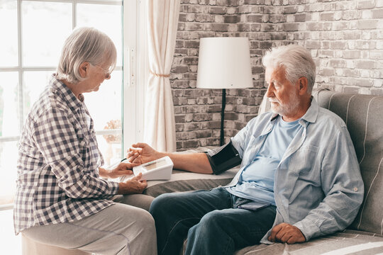 Senior woman using medical device to measure blood pressure of her husband suffering of hypertension - elderly couple sitting at home on sofa takes care of health - Powered by Adobe