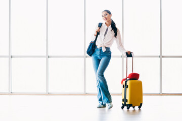 Charming woman casually dressed with jeans and a yellow suitcase standing in an airport terminal...