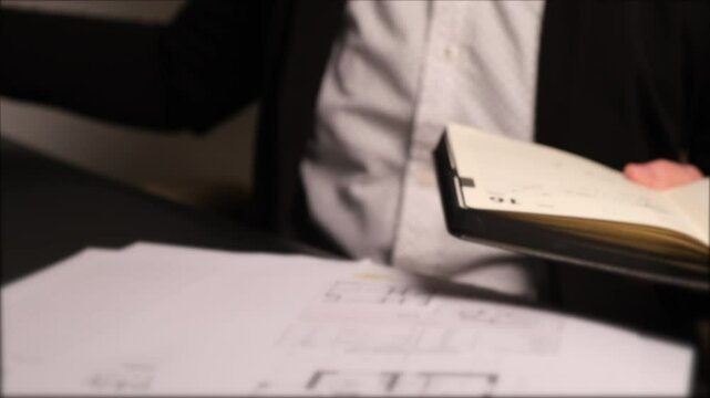 An unrecognizable realtor worker at the table sorts through papers and documents, a house plan or construction