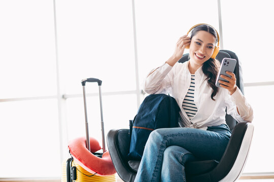 Young woman with headphones enjoying leisure time at the airport while using smartphone and traveling in style.