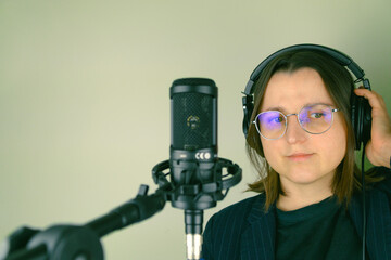 Female podcaster with headphones and microphone in recording studio