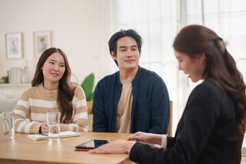 Young Asian couple attentively listening to professional female consultant during meeting at home.