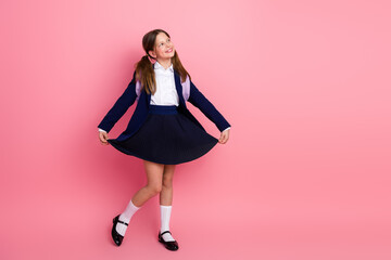 Cheerful schoolgirl posing in a neat uniform on pink background, carrying backpack, emphasizing...