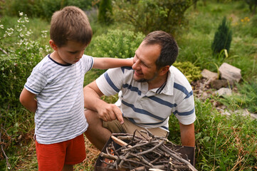 father and son light a fire for barbecue, collect brushwood and put it in the grill in the summer...