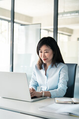 Korean middle-aged woman using computer for financial bank work online. Mature Asian professional specialist businesswoman working on laptop pc sitting at desk in office looking at screen. Vertical