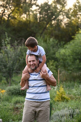 Happy father and  son playing outside in garden in summer in sun. dad roll son on neck, roll on...