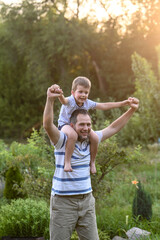 Happy father and  son playing outside in garden in summer in sun. dad roll son on neck, roll on...