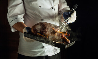 A chef in a white uniform holds a black tray filled with sizzling grilled meat. The steam rises,...