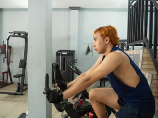 young sports indonesia asian man in blue cycling in fitness center. Cardio workout, leg workout,...