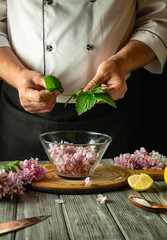 A chef adds mint leaves to acacia flowers in a bowl to make a delicious kvass. The concept of...