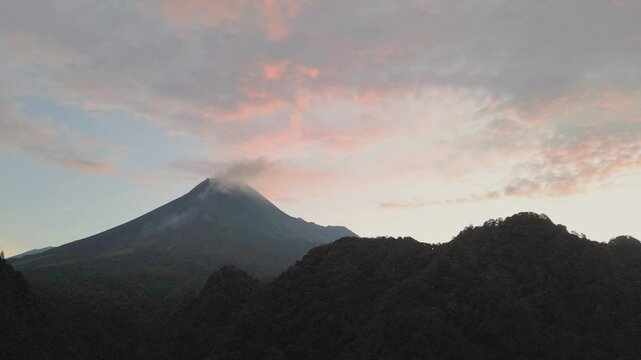 Drone view of Mount Merapi under a sky brushed with soft sunset hues over dark hills