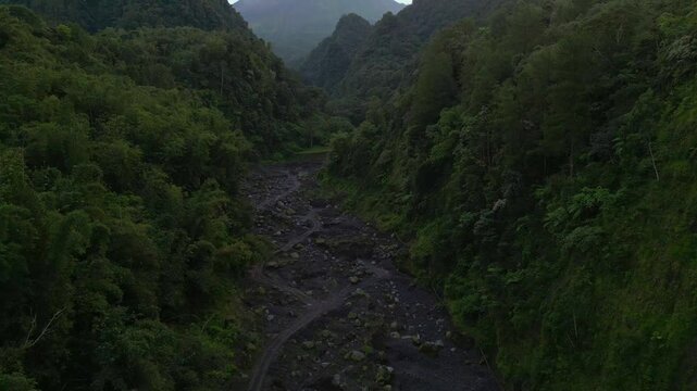 Mount Merapi above a lush, forested valley with a dry riverbed in Central Java, Indonesia