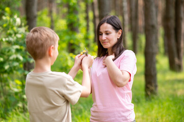 Obraz premium Boy giving a flower to his mother in a sunny forest clearing, tender family moment in nature