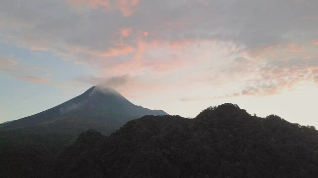 Drone view of Mount Merapi under a sky brushed with soft sunset hues over dark hills