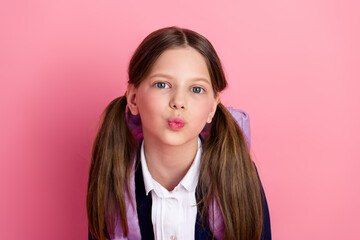 Portrait of a young schoolgirl with ponytails smiling against a pink background, ready for studies...