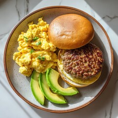 A delectable breakfast sandwich featuring fluffy scrambled eggs, ripe avocado slices, and juicy sausage patty on a fresh bun, served on a ceramic plate with natural lighting.