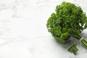Bunch of fresh parsley on white marble table, closeup. Space for text