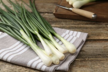 Fresh ripe green onions and towel on wooden table, closeup