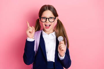 Smiling preteen schoolgirl holding light bulb concept idea while wearing uniform standing against pink background