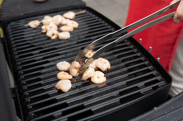 Caucasian adult grilling shrimp outdoors with metal tongs