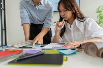Two Asian women working together in a bright, modern studio.while using a laptop and smartphone....