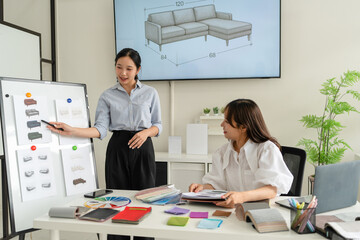 Two Asian women working together in a bright, modern studio.while using a laptop and smartphone....