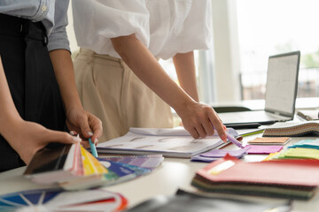 Two Asian women working together in a bright, modern studio.while using a laptop and smartphone....