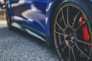 Close-up of a sports car alloy wheel with red brake caliper and detailed finish on a metallic blue...