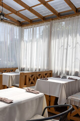Bright outdoor cafe terrace with wooden tables and curtains
